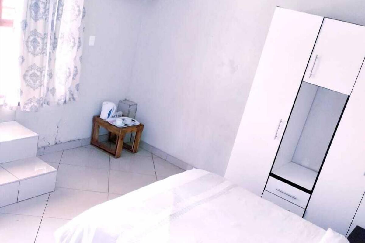 Un dormitorio con cama, armario, una mesita con silla y un aire acondicionado.