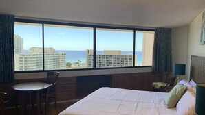 Una camera d'albergo con un'ampia finestra, un letto, una scrivania e una sedia.