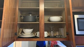 Un armadietto da cucina in legno con ripiani che contengono una pentola, un colapasta, piatti, un bicchiere da vino e bicchieri.