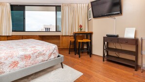 A hotel room with a bed, a desk with a chair, a TV mounted on the wall, and a window with curtains. - Free Parking! 40th Floor Penthouse Studio with Stunning View (Honolulu)