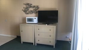 A room with a beige wall, a flat-screen TV on a cabinet, a microwave, and a decorative wall piece. - Studio in the Middle of Waikiki, Short walk to beach (Honolulu)
