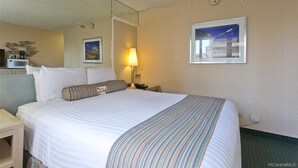 A hotel room with a large bed, a bedside table, a lamp, a framed picture on the wall, and a microwave on a counter. - Studio in the Middle of Waikiki, Short walk to beach (Honolulu)