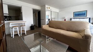 Una habitación de hotel compacta con kitchenette, sofá, una mesita de centro de vidrio y cama.