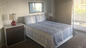Un dormitorio con cama, dos mesitas de noche, cómoda y un cuadro en la pared, además de vistas al exterior.