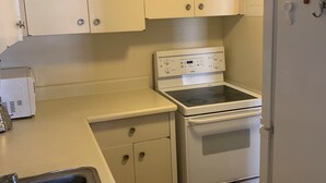 Una cocina compacta con armarios blancos, horno integrado, refrigerador y pileta.