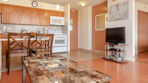 A modern kitchen with wooden cabinets, a microwave, and a dining area with a table and chairs. - 29th Floor Waikiki Banyan, Full Kitchen and Free Parking (Honolulu)