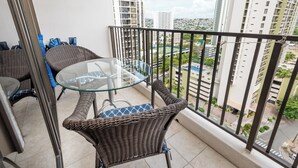 Un balcón con mobiliario de mimbre, una mesa de vidrio y vistas a un paisaje urbano.
