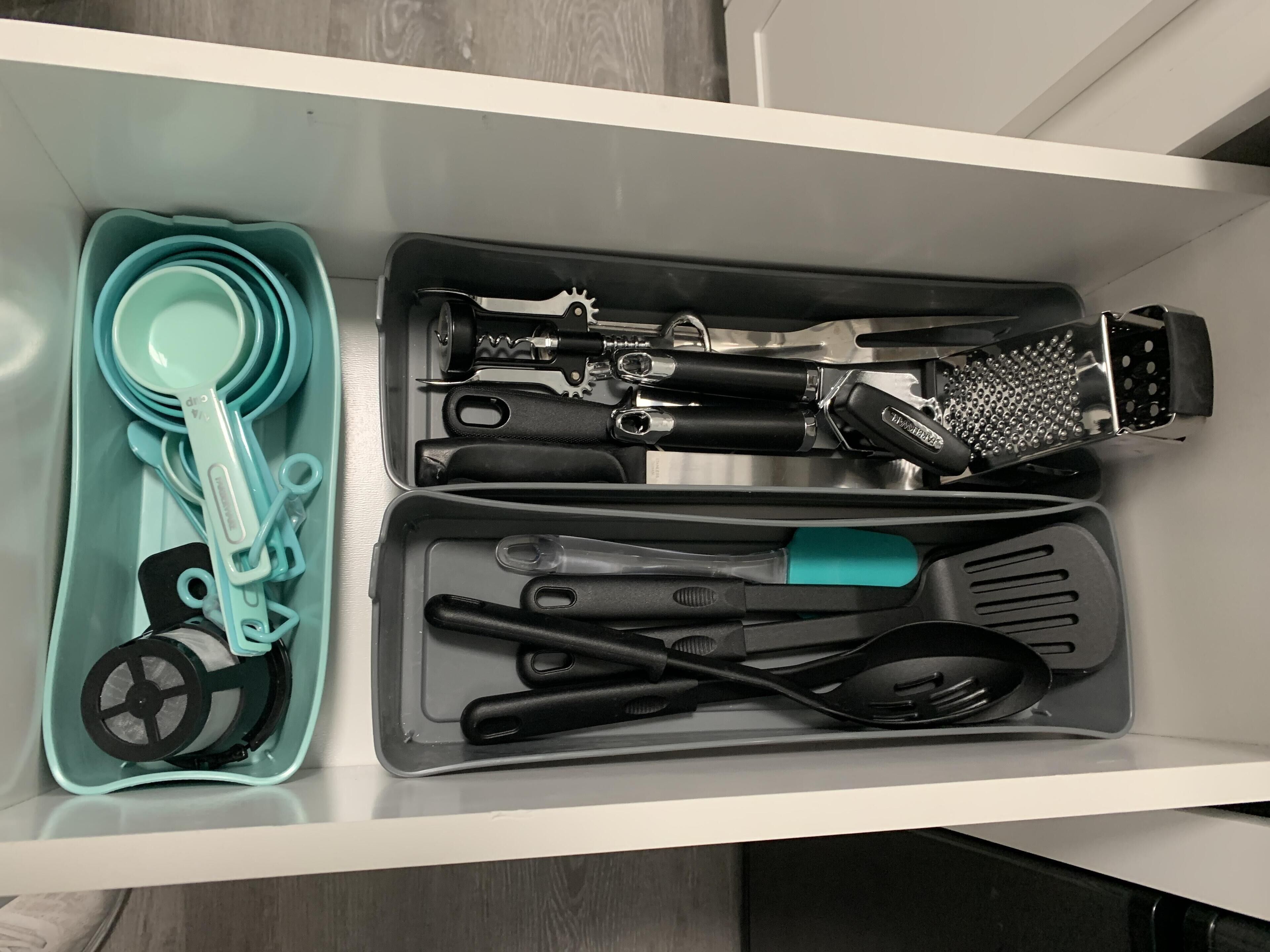 Un tiroir de cuisine contenant divers ustensiles et outils de cuisine, notamment des tasses à mesurer, une râpe et une spatule.