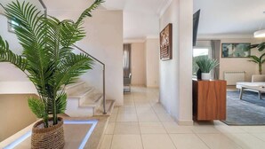A modern interior with a staircase, a large potted plant, a wooden cabinet, and a painting on the wall.