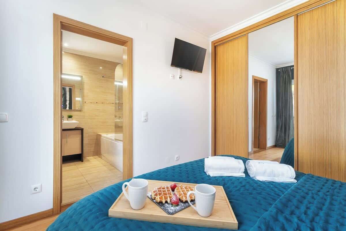 Camera d'albergo con un letto, una TV a muro e un vassoio per la colazione con waffle e tazze da caffè.