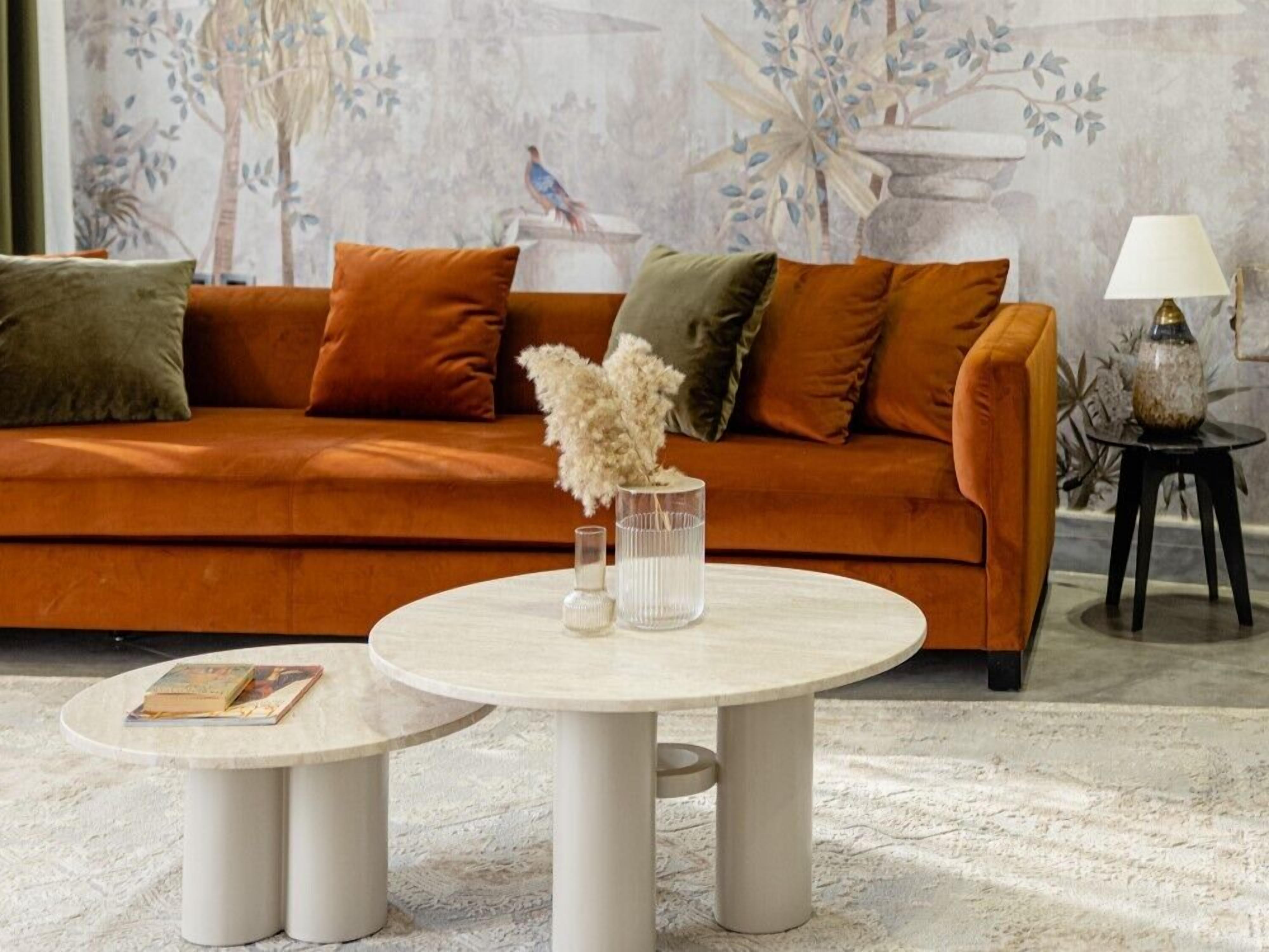 Un salon avec un canapé, deux tables rondes et un vase contenant des fleurs séchées.