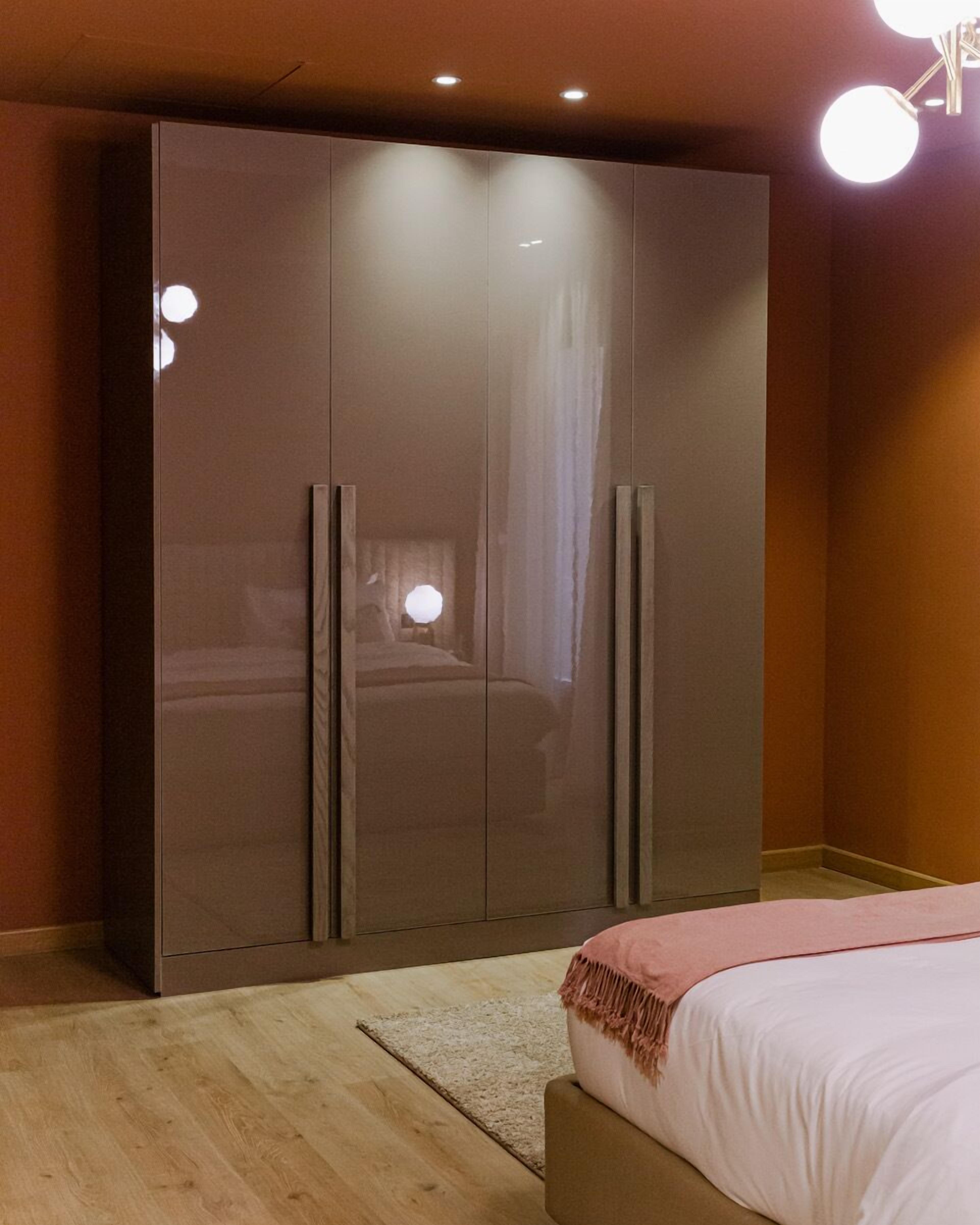 A bedroom with a large wardrobe, a bed with a pink blanket, and a wooden floor.