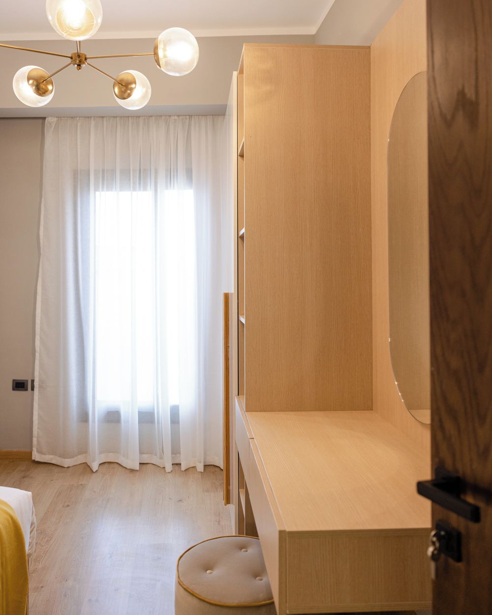 A room with a wooden wardrobe, a round mirror, and a light fixture with multiple bulbs.