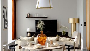 Een moderne woonkamer met een ronde eettafel, zwarte stoelen, een bank, een televisie en een grote vaas met bloemen.