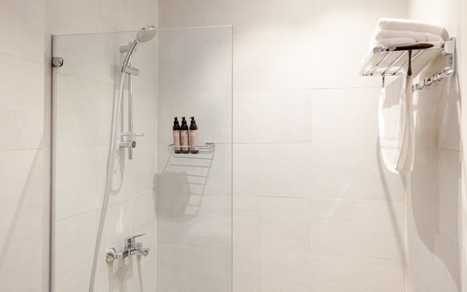 A modern shower with a glass door, a towel rack with folded towels, and a shelf with toiletries.
