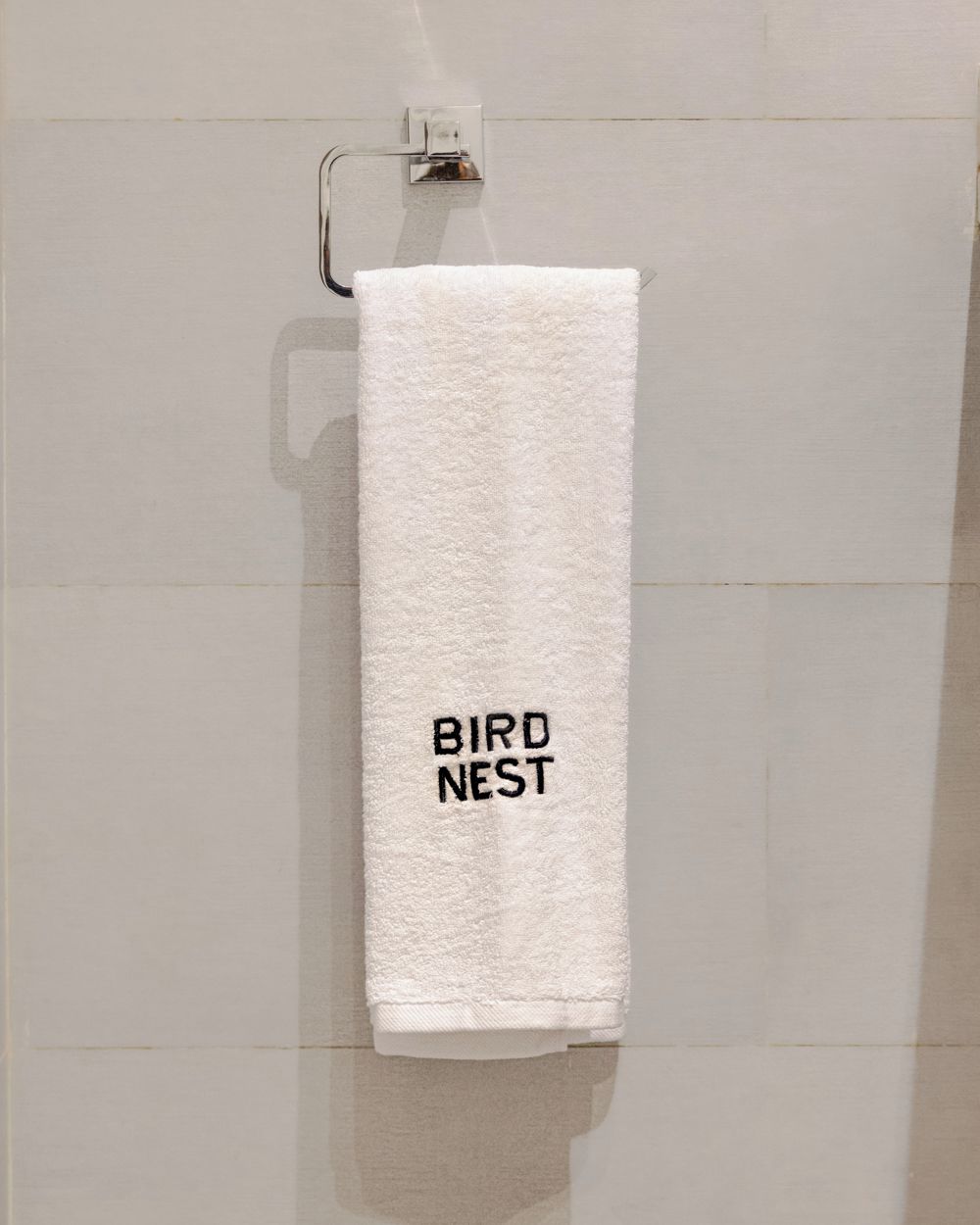 A white towel hanging on a metal towel rack in a bathroom with plain tiled walls.