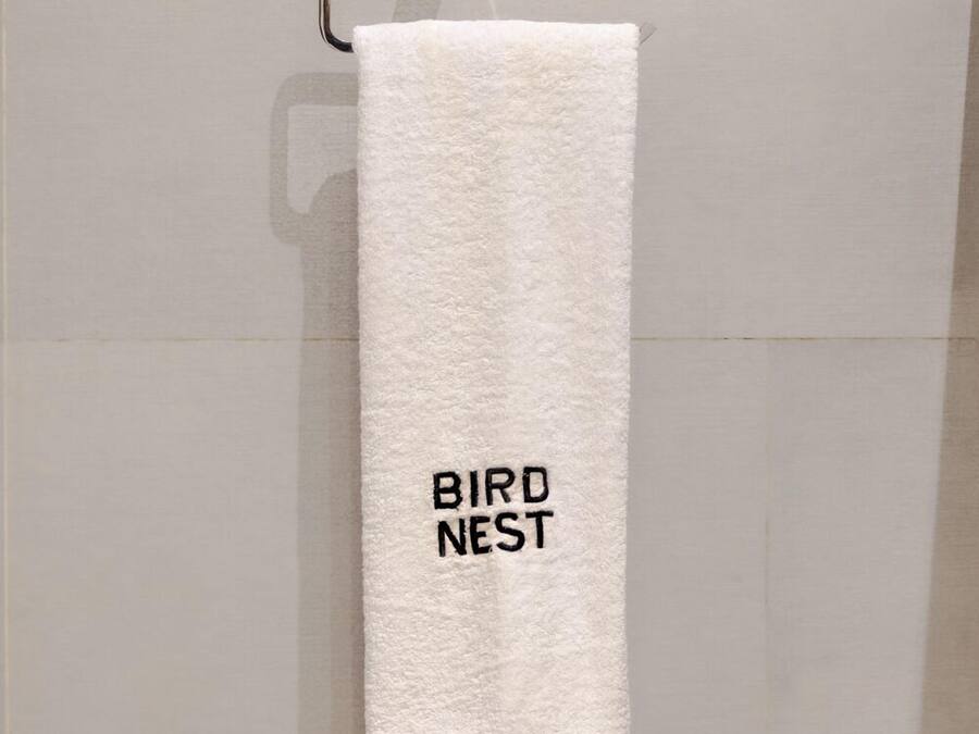 A white towel hanging on a metal towel rack in a bathroom with plain tiled walls.