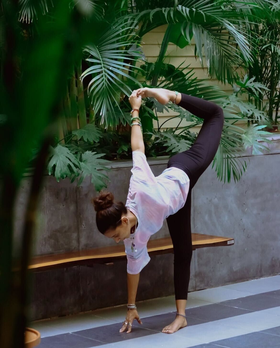Una persona realiza una postura de yoga al aire libre, con abundante vegetación verde de fondo.