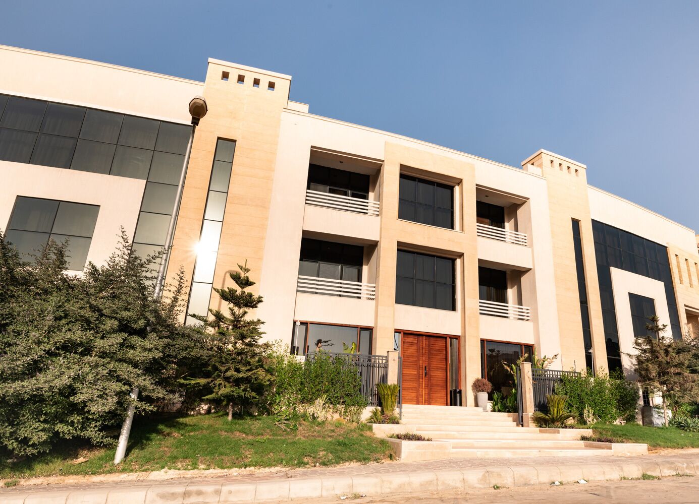 A modern multi-story building with a symmetrical facade, large windows, and a central entrance with a wooden door.