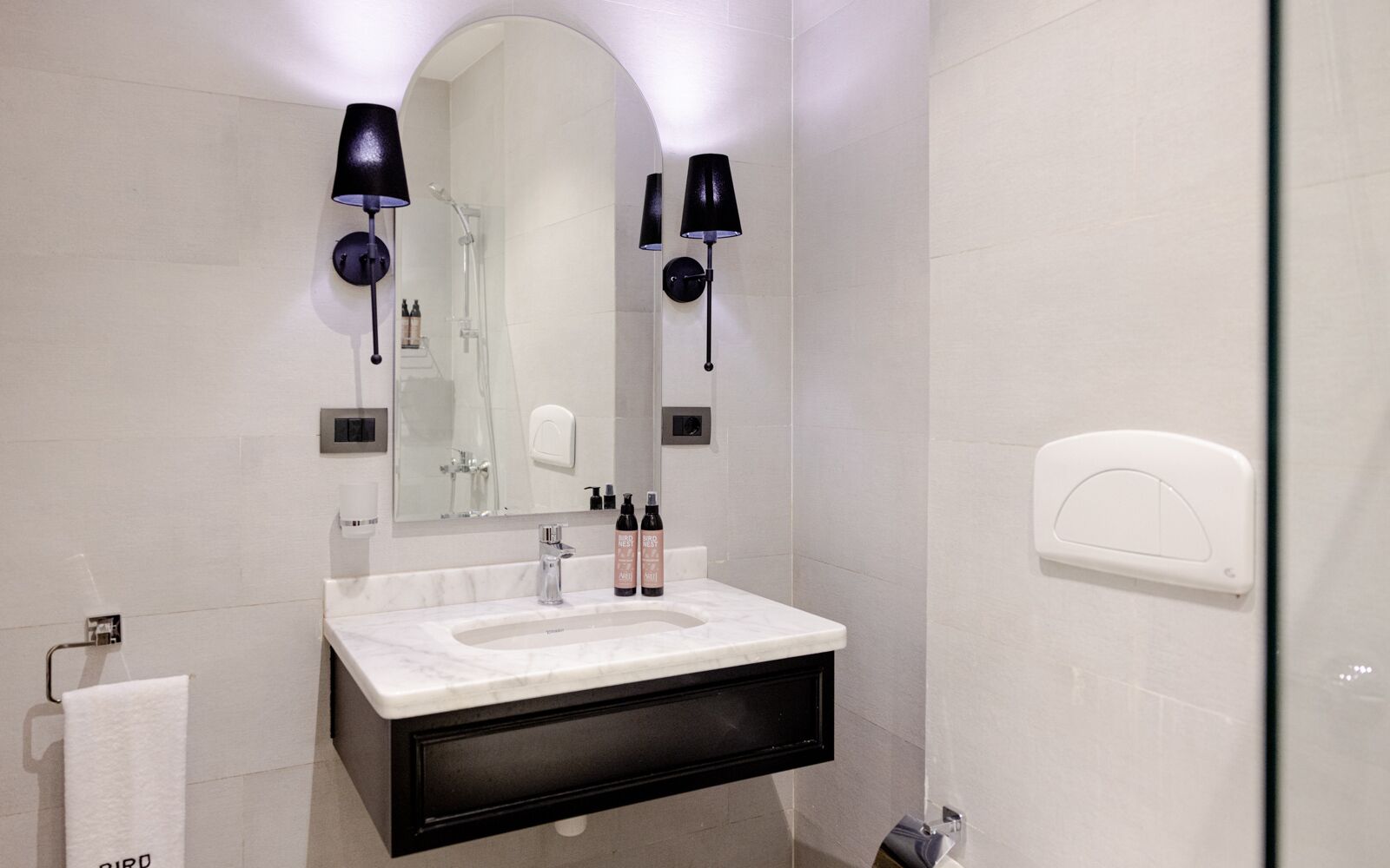 A modern bathroom with a white sink, black vanity, and two black wall-mounted lamps.