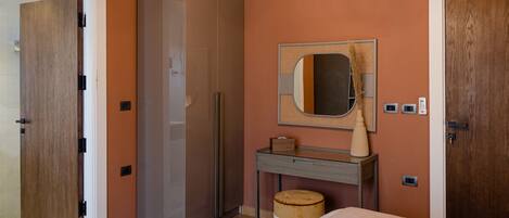 A bedroom with a wardrobe, a vanity with a mirror, a bedside table, and a bed.