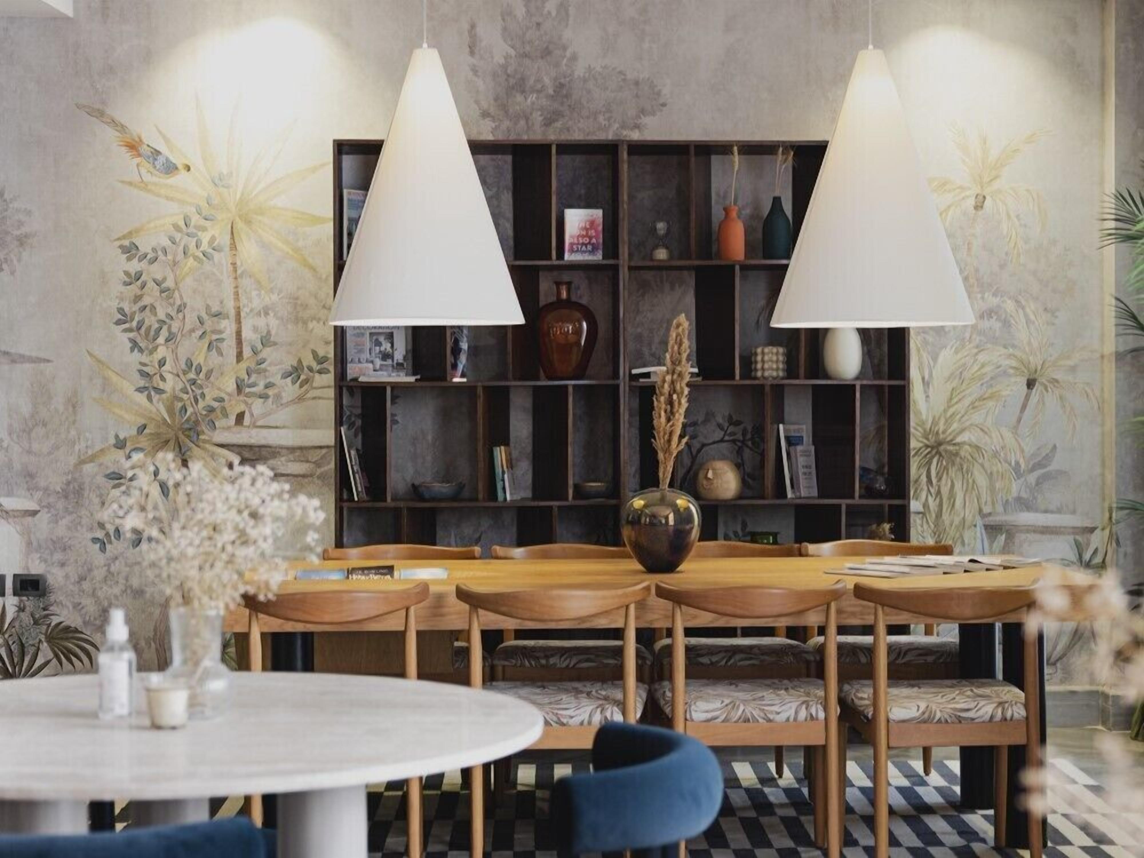A dining area with a round table and six wooden chairs, a bookshelf in the background, and two pendant lights.