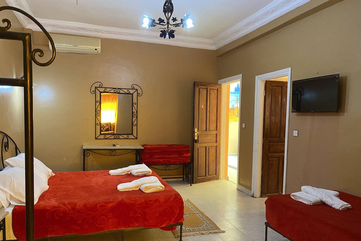 A hotel room with two beds, a mirror, a television, and a door leading to another room.