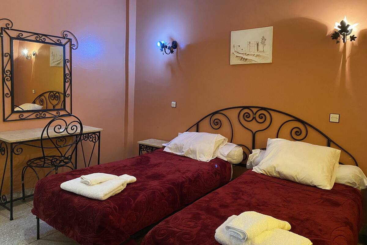A room with two beds, a desk, a mirror, and wall-mounted lights.