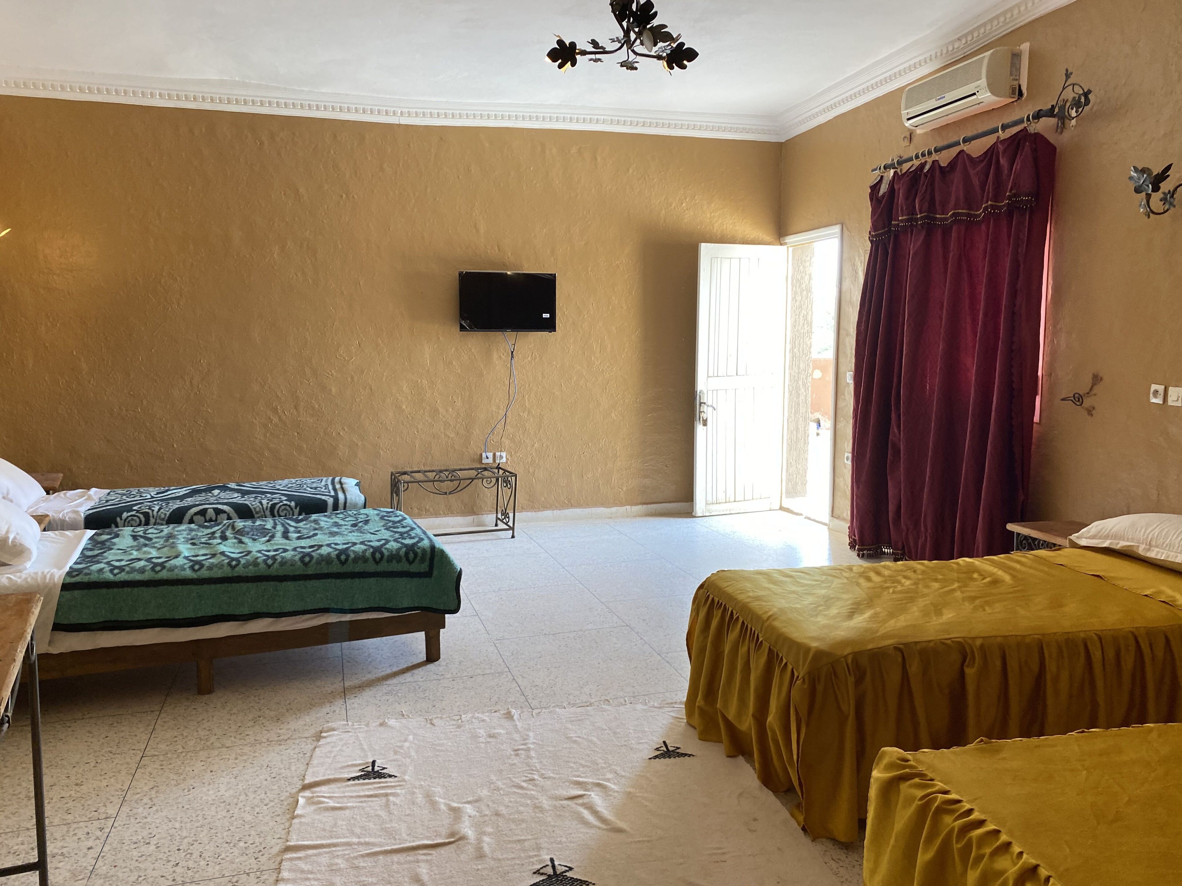 A hotel room with two beds, a television, an air conditioning unit, and a view of the outside through an open door.