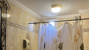 A bathroom with a toilet, a sink, a shower curtain with floral patterns, a hand dryer, and a light fixture on the ceiling.