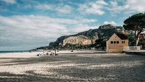 A beach with a small building, clear skies, and a mountain in the background. - Palazzo Liberty (Palermo)