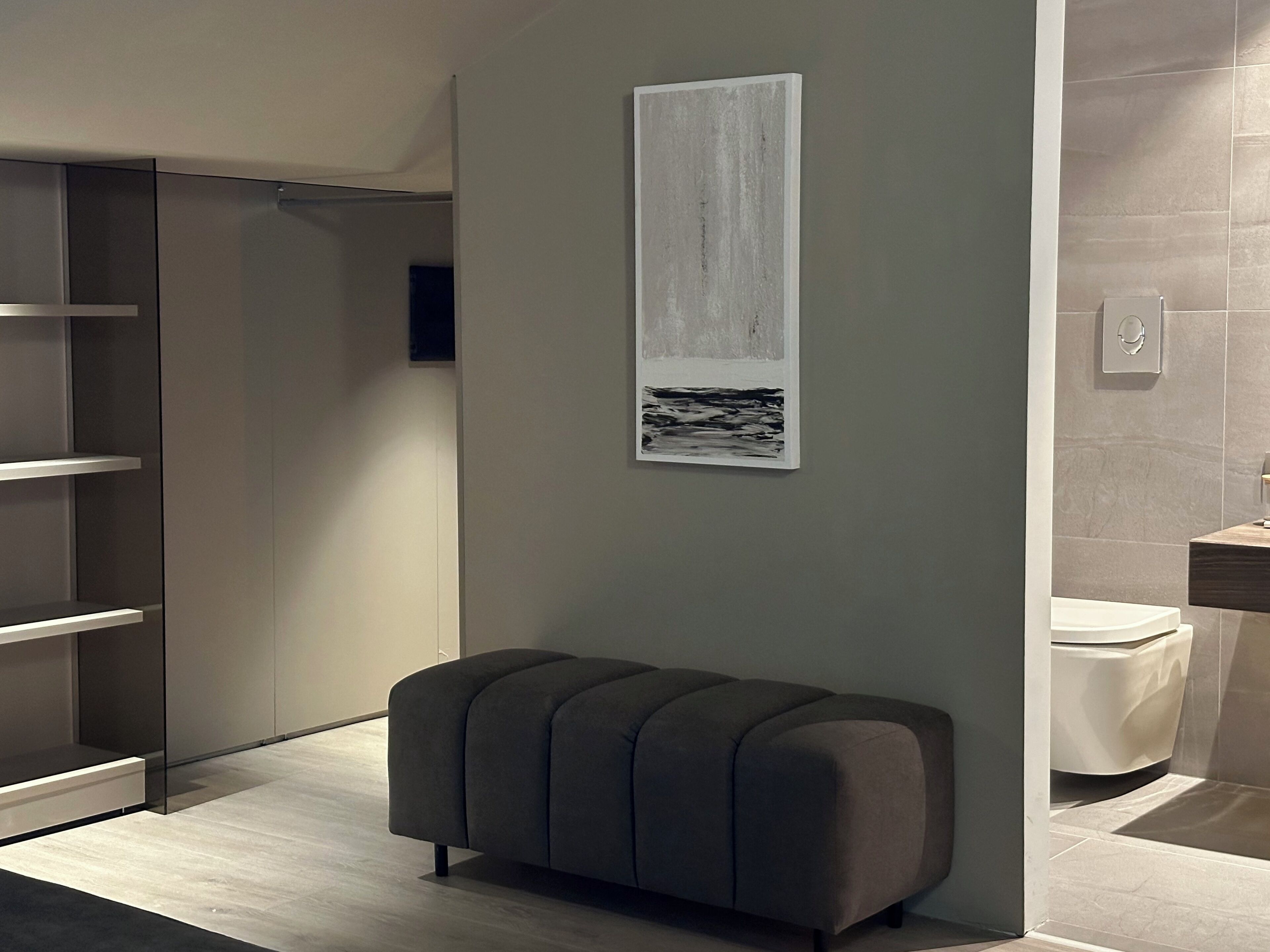 Een moderne badkamer met een grijze bank, een groot kunstwerk aan de muur en een toilet.