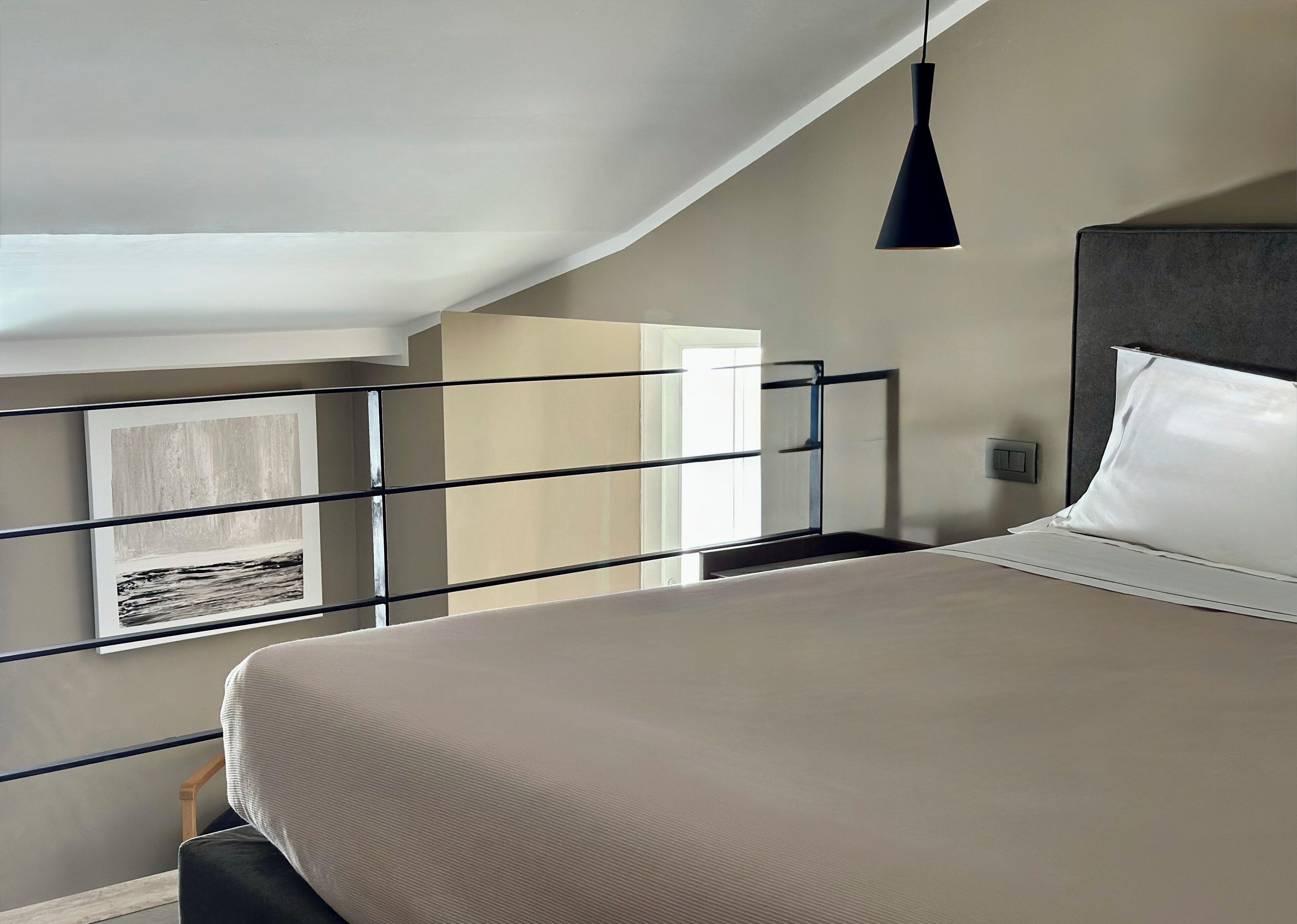 A bedroom with a bed, a hanging light fixture, a window with a view, and a door.