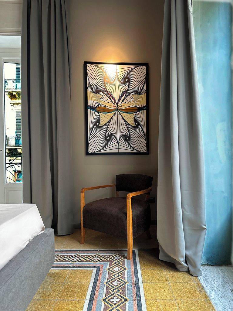 Une chambre d’hôtel moderne, équipée d’un lit, d’une chaise, d’une œuvre d’art décorative au mur et d’un tapis à motifs.