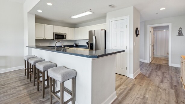 A modern kitchen with white cabinets, stainless steel appliances, and a central island with bar stools. - Ocean Park 114 - Hosted by Moore AI Rentals (Fernandina Beach)