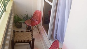 A small balcony with two red plastic chairs, a woven bench, and a potted plant. - Lux Suites La Vida Studio Apartment (Mombasa)