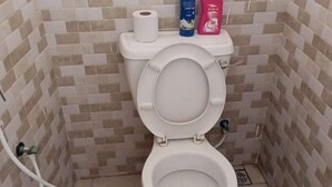 A small, tiled bathroom with a toilet, a roll of toilet paper, and two toiletry bottles on the tank. - Lux Suites La Vida Studio Apartment (Mombasa)