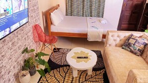 A small, cozy room with a bed, a sofa, a TV, and a coffee table. - Lux Suites La Vida Studio Apartment (Mombasa)