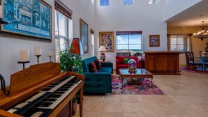 A spacious living room with a grand piano, a blue sofa, a red sofa, and a dining area with a chandelier. - Condo 40-4 El Dorado Ranch (San Felipe)