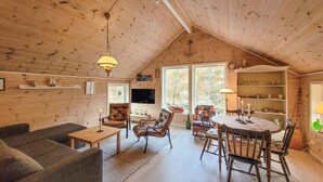 Interior acogedor de una cabaña con techo de madera, una mesa de comedor con sillas, un sofá y un televisor.