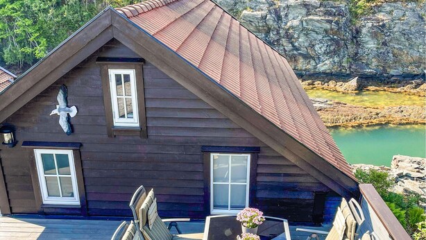 Una cabaña de madera con techo inclinado, dos ventanas y un porche con mobiliario exterior.