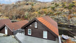 Una cabaña con techo inclinado, fachada de madera y un muelle que se adentra en el agua.