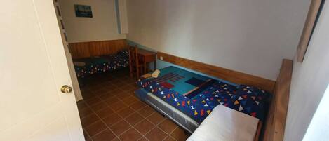 A small, compact room with two beds, a wooden headboard, a small table, and a door.