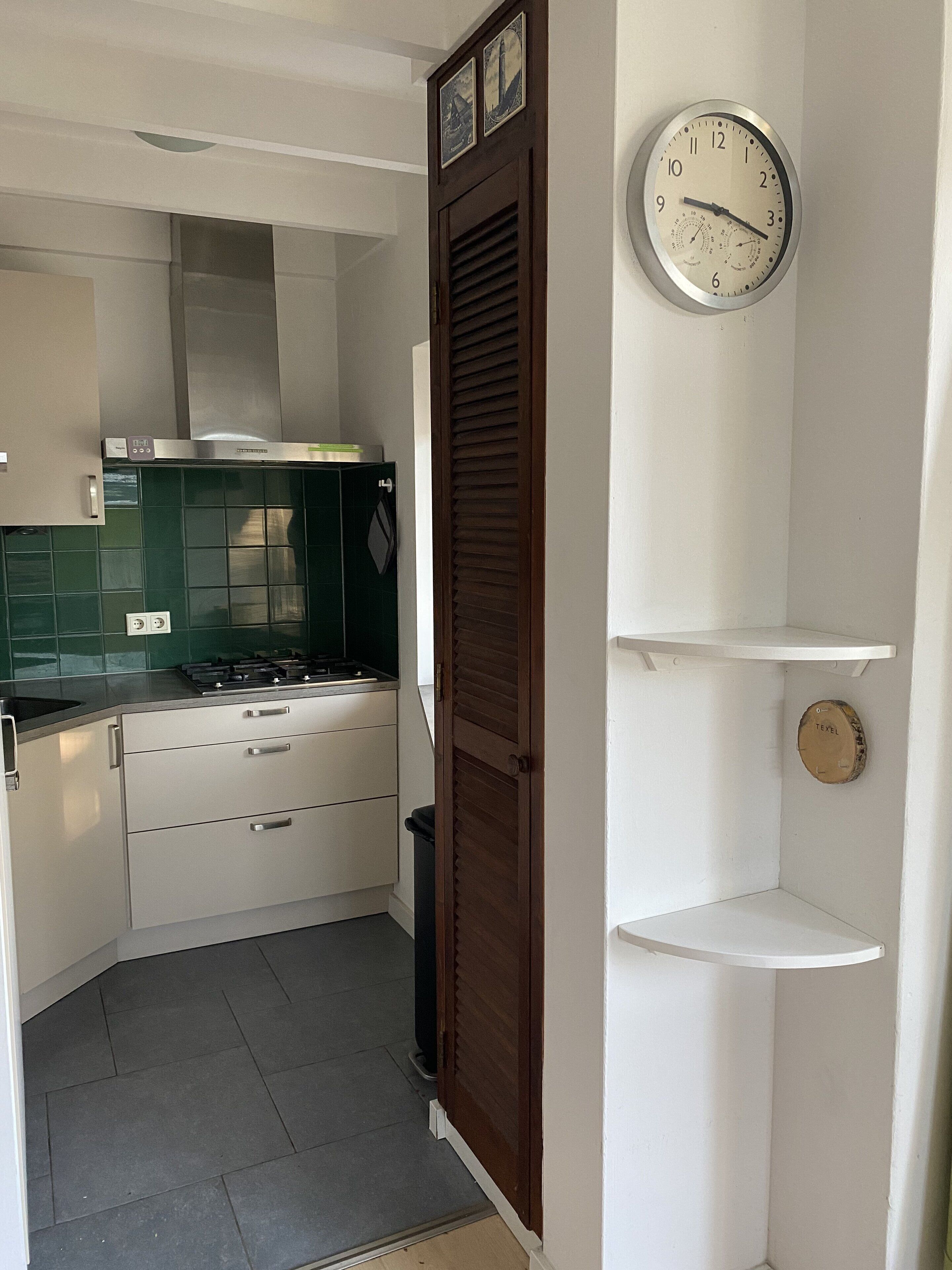 Een moderne keuken met een gasfornuis, witte kastjes en een klok aan de muur.