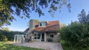 Une maison à deux étages, avec un toit en tuiles, une terrasse dotée d’une table et de chaises, et une véranda en verre.