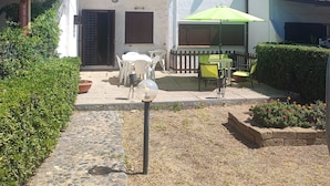 A two-story building with a white exterior, a tiled roof, and a small patio area with outdoor furniture and a green umbrella. - Villa 100 steps from the beach (CIN It092066C2000R5478) (Sardegna)