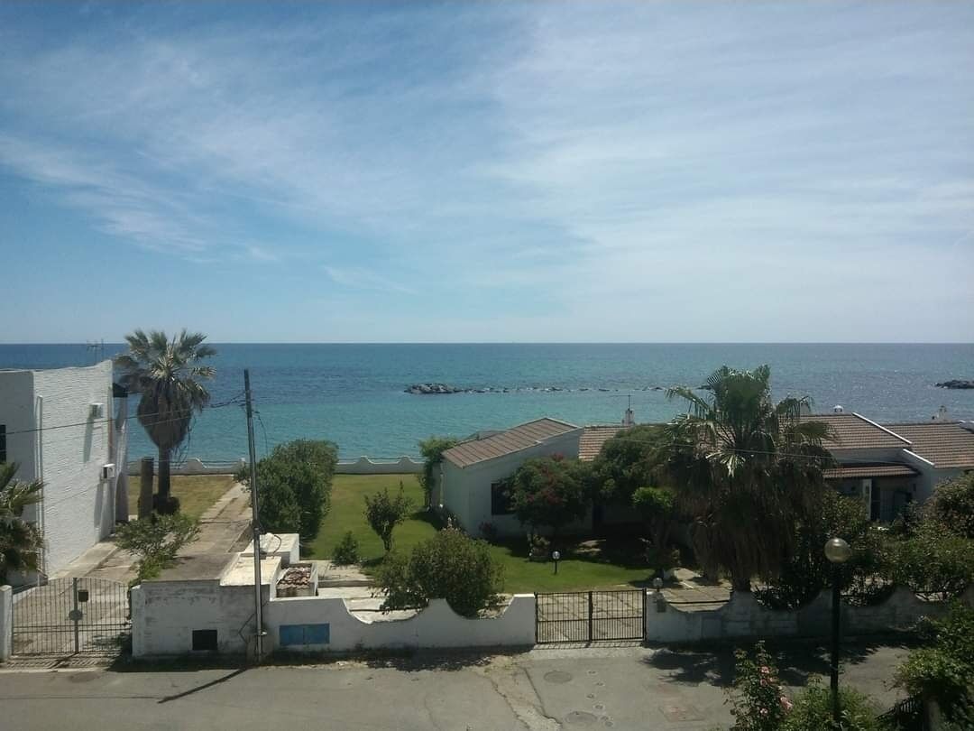 A coastal residential area with houses, a clear sky, and the sea in the background.