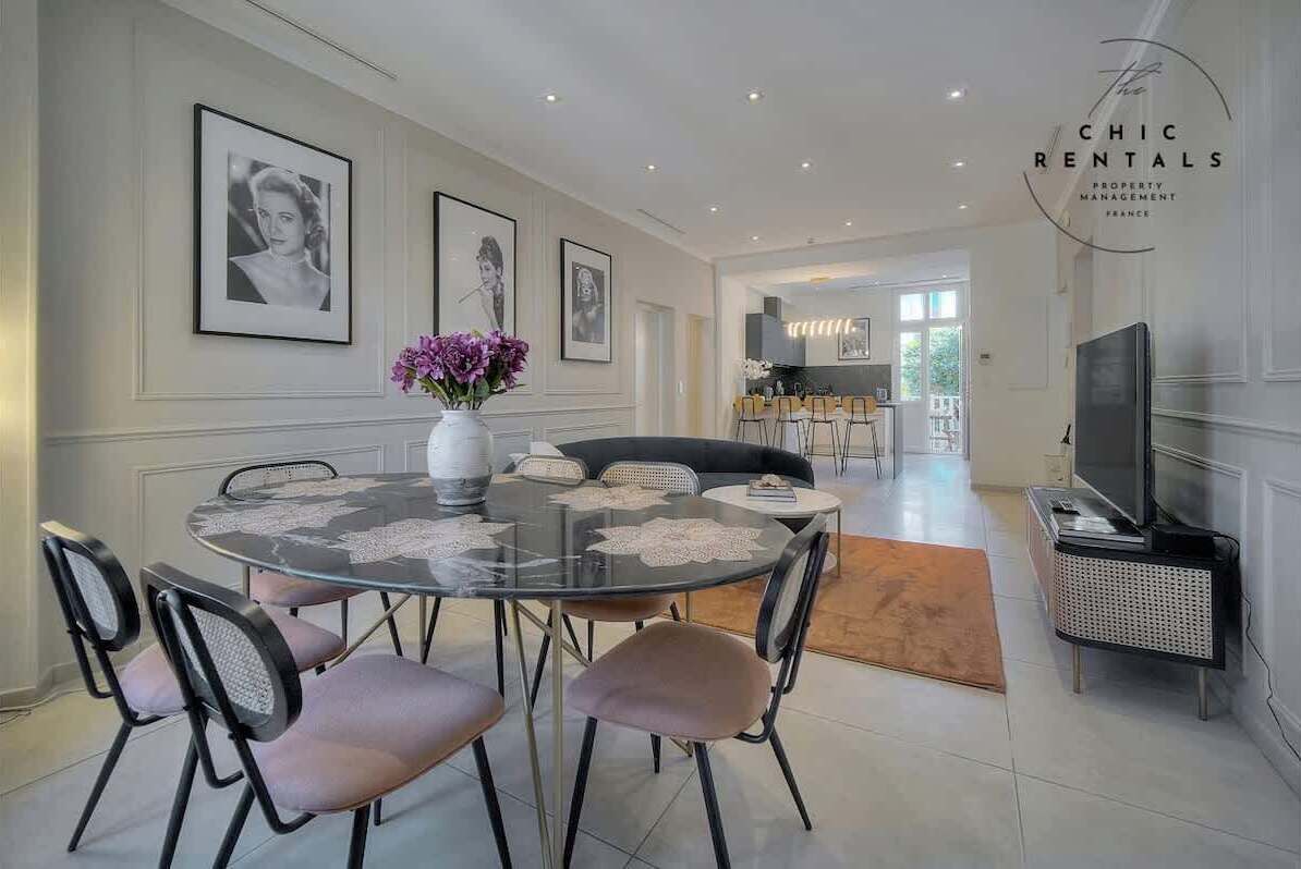 A dining area with a round glass table, cushioned chairs, and framed artwork on the walls.
