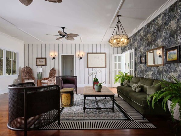 A living room with a sofa, chairs, a coffee table, a patterned rug, and a ceiling fan.
