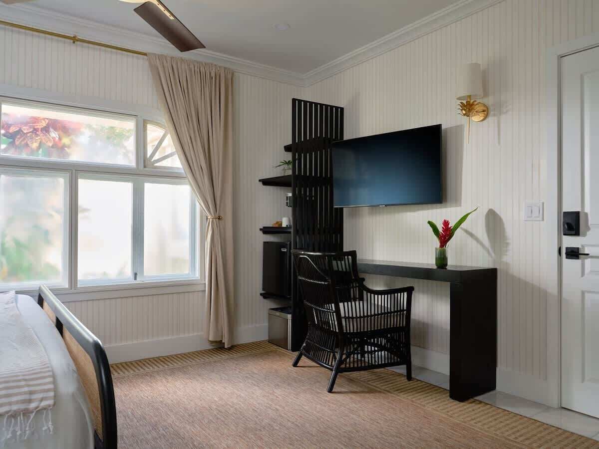Ein Schlafzimmer mit einem Bett, einem Schreibtisch mit Stuhl, einem Fernseher und einem Fenster mit Vorhängen.